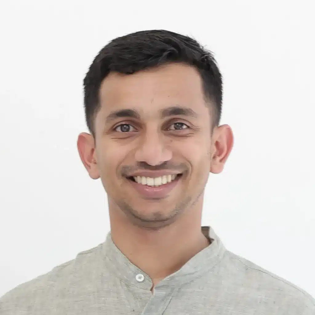 Smiling man wearing a light gray traditional shirt against a white background, showcasing a friendly and approachable demeanor.